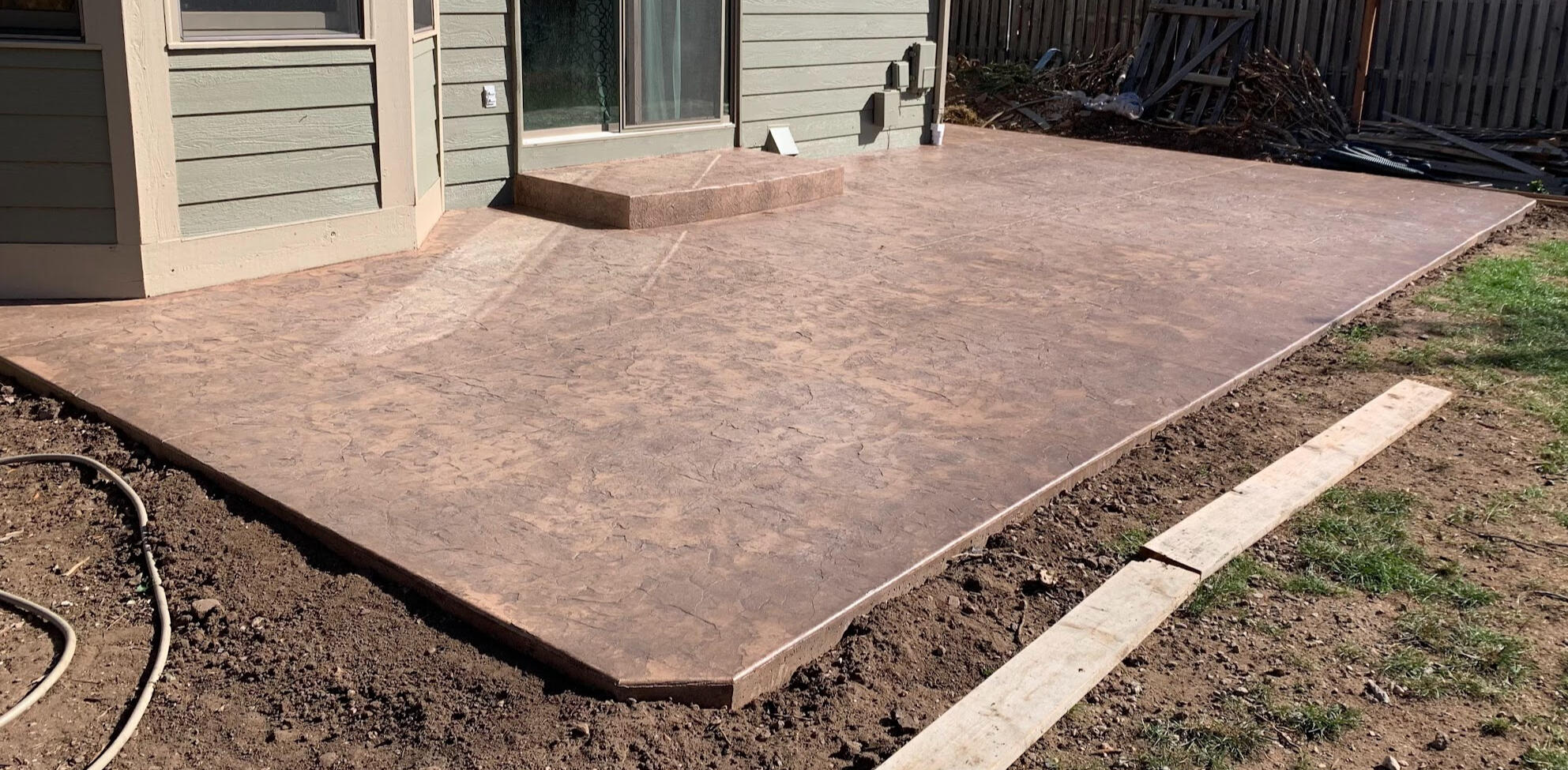 Stamped concrete backyard patio in Fort Collins, Colorado with a warm brown finish and rock stamped pattern for outdoor living.