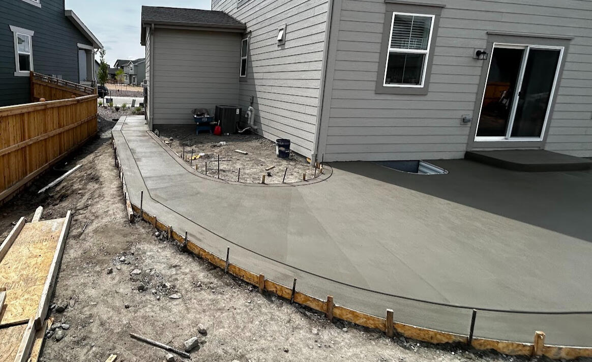 Curved concrete walkway in Timnath, CO with a smooth broom finish, providing durable access along the side of a home