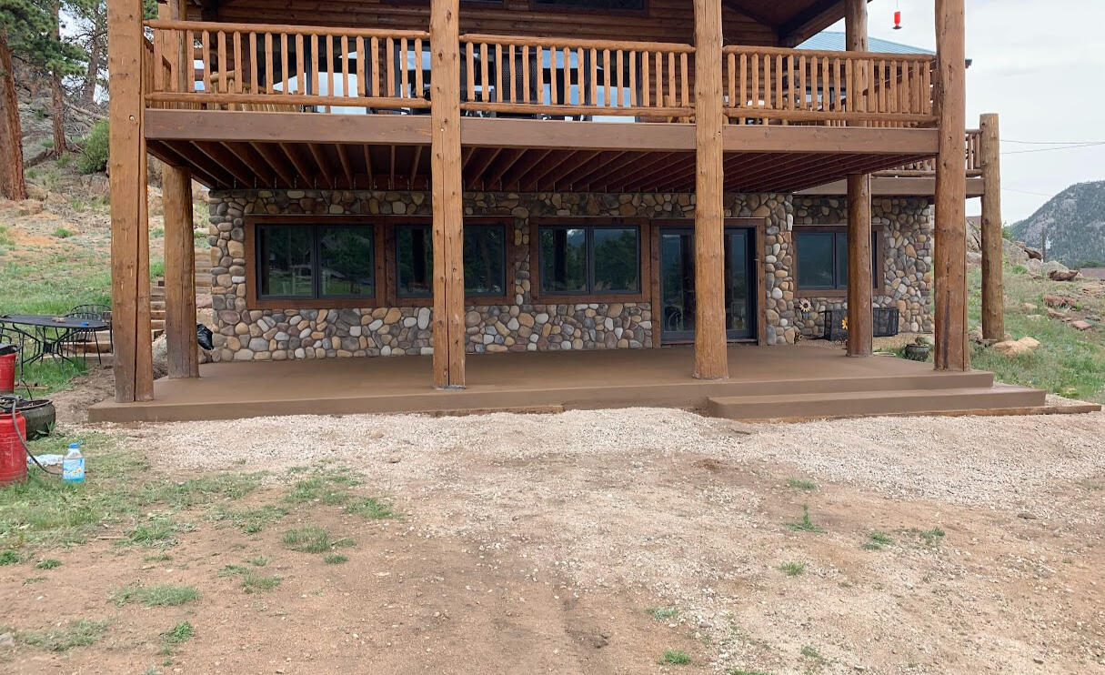 Colored concrete patio in Fort Collins, CO with a rich brown finish, installed beneath a rustic wood deck for outdoor living