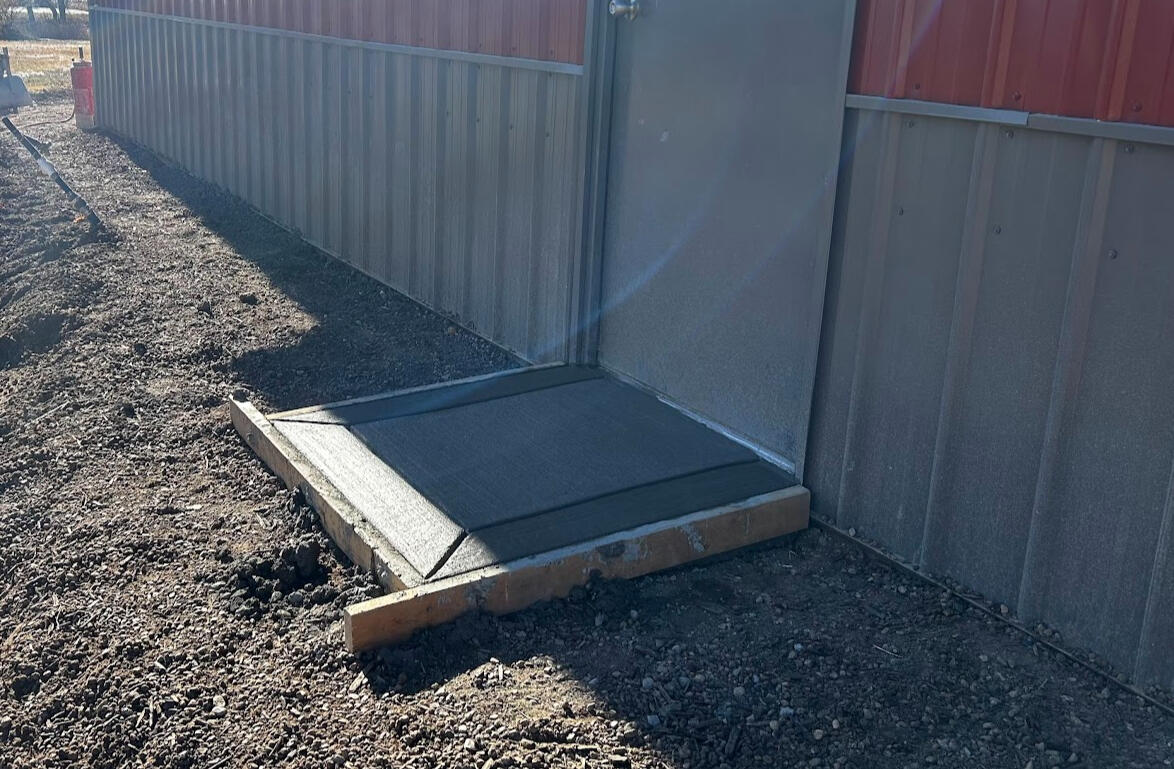 Freshly poured concrete patio slab with control joints next to metal shop building, Fort Collins area.”