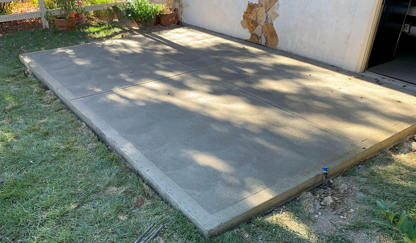 Backyard concrete hot tub slab with smooth broom finish and clean edges near house exterior.
