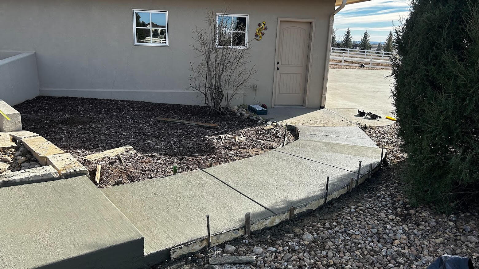 Curved concrete sidewalk with broom finish leading to side door of home, bordered by landscaping and rock bed