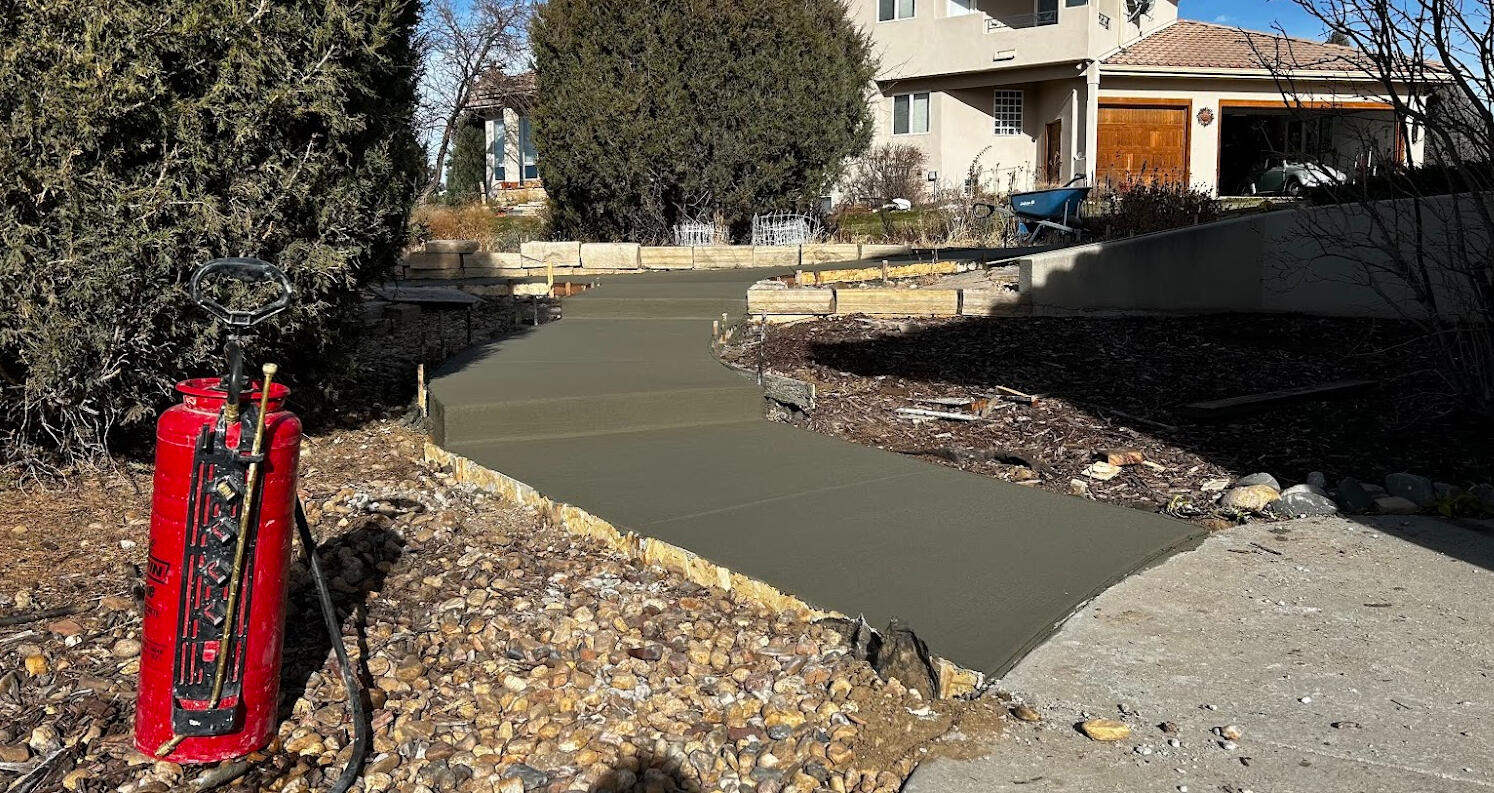 Newly poured curved concrete walkway with step transition to sloped yard