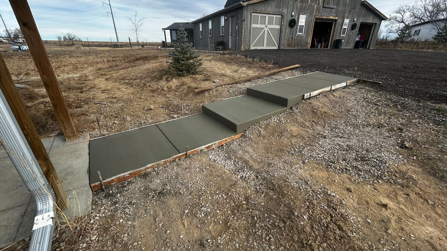 New concrete walkway with integrated steps in Berthoud, CO on sloped ground leading to barn-style building in rural setting