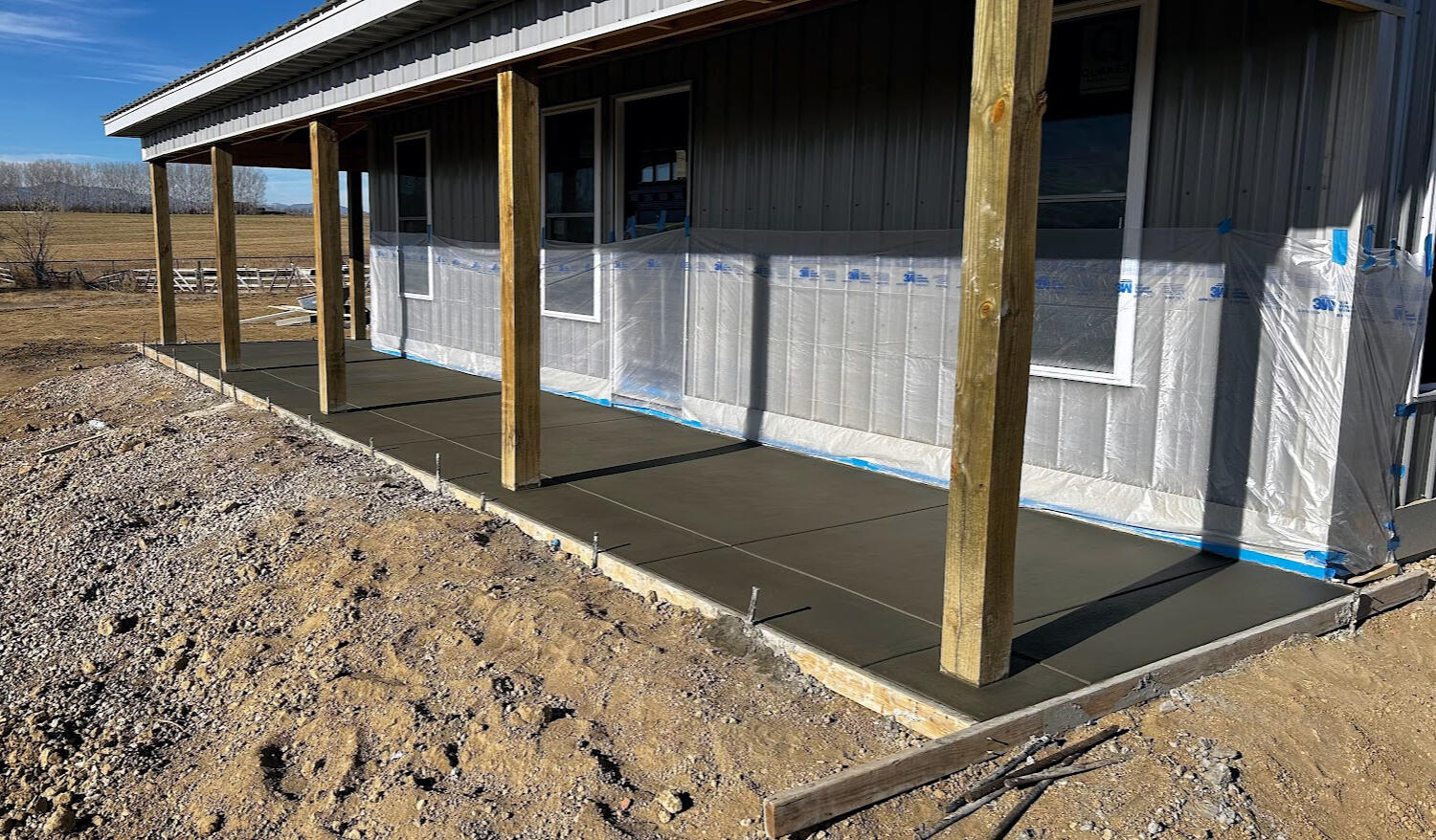 Freshly poured concrete front porch slab on barndominium with wooden posts in Berthoud, CO