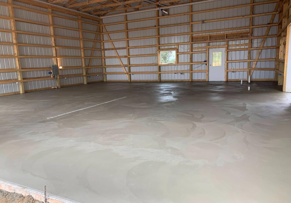 Freshly finished concrete floor with a built in drain inside large barn or workshop with a smooth trowel finish