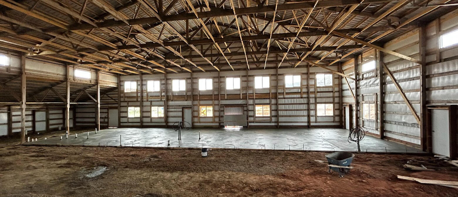 Freshly poured concrete floor inside large agricultural barn, wide view showing slab with a smooth trowel finish