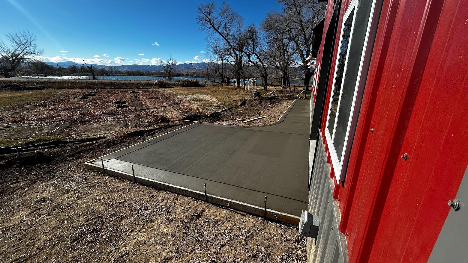 New concrete patio slab along red post framed barn in Berthoud, Colorado.