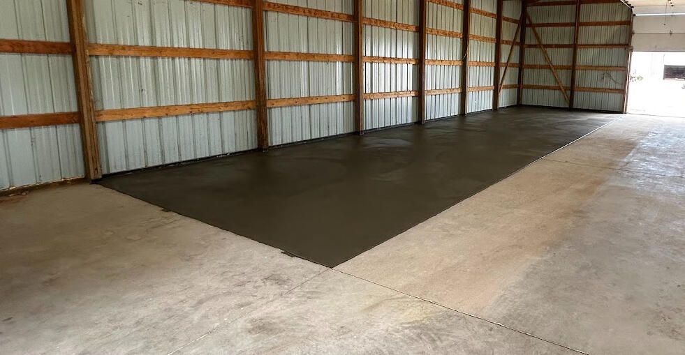 New concrete floor section poured inside large barn building, smooth finish contrasting with existing slab in Wellington, CO