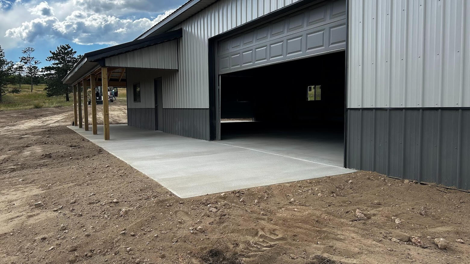 Fresh concrete driveway apron and side porch slab outside metal shop with open garage door and clean edges in Bellvue, CO