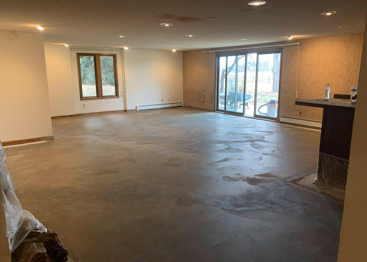 Concrete floor poured in large open basement living area with sliding glass door and recessed lighting, in Wellington, CO