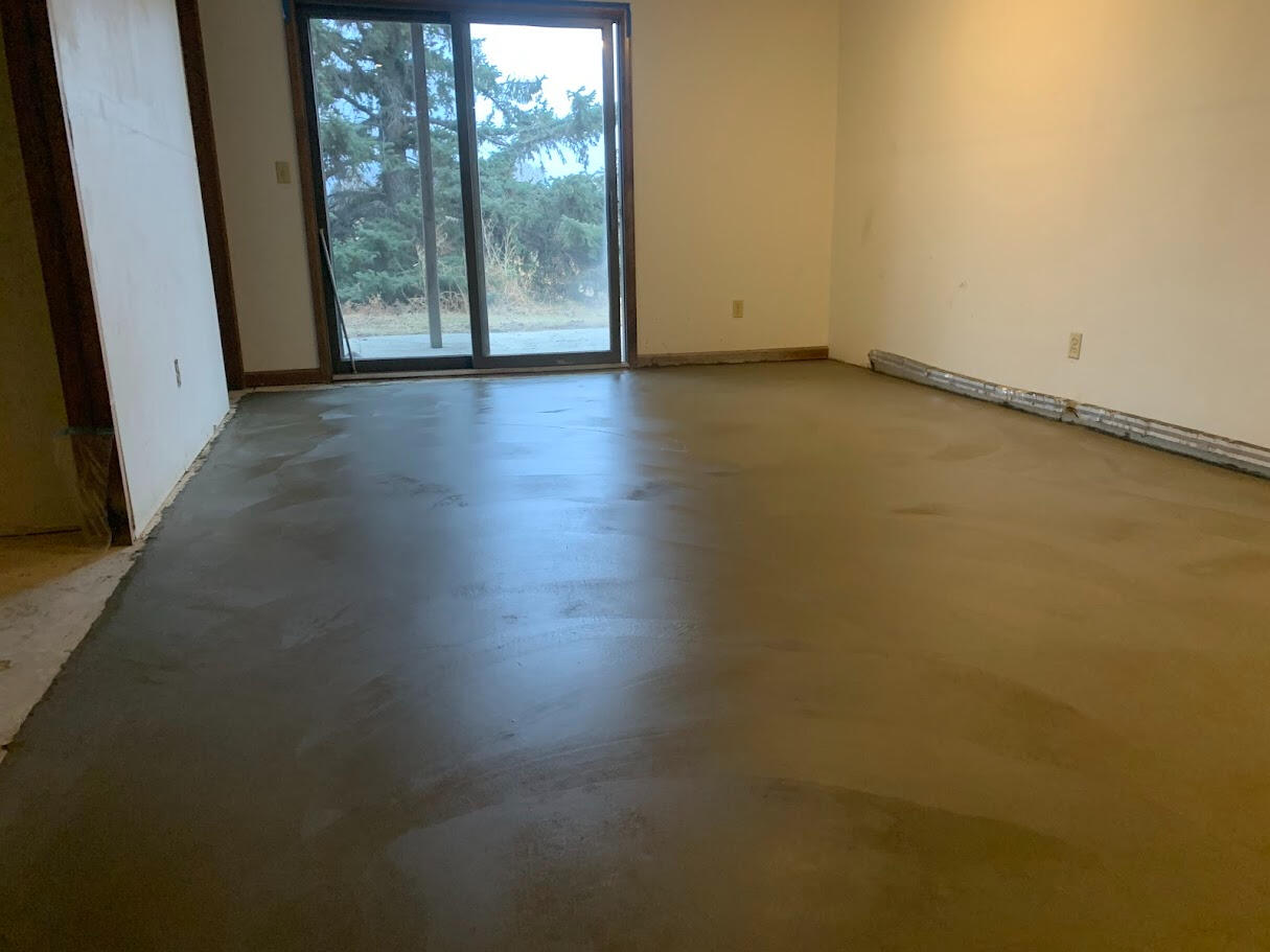 Freshly finished concrete basement floor in residential room with sliding glass door and natural light in Wellington, Colorado.
